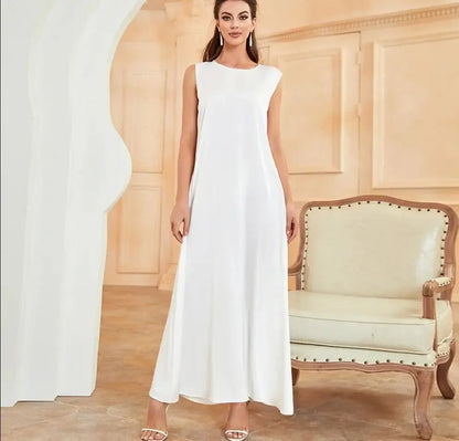 Woman wearing a white Ramadan inner dress for modest Islamic fashion, standing beside a vintage chair in a beautifully decorated room