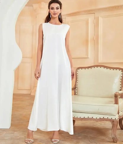 Woman wearing white Ramadan inner abaya dress, standing indoors next to a chair.