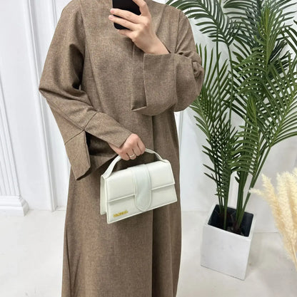 Woman wearing a Closed Linen Abaya in a sophisticated setting, holding a stylish white handbag.